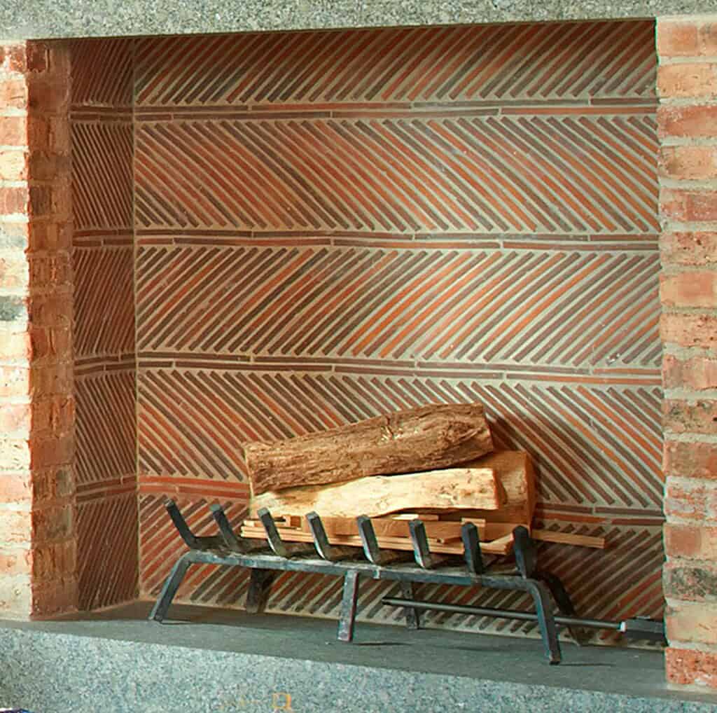 Fireplace interior lined with reclaimed clay roof tiles in a herringbone fireback pattern, showcasing heat resistance and rustic design